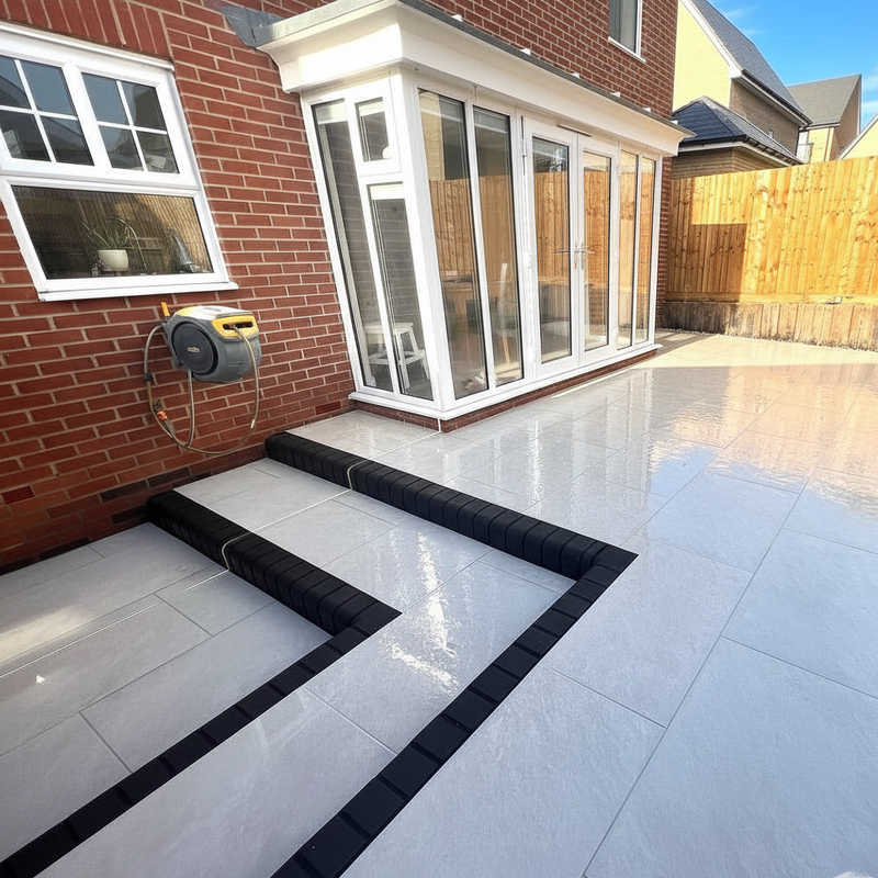 Load image into Gallery viewer, Modern patio area with white tiles and black border, adjacent to a brick building.
